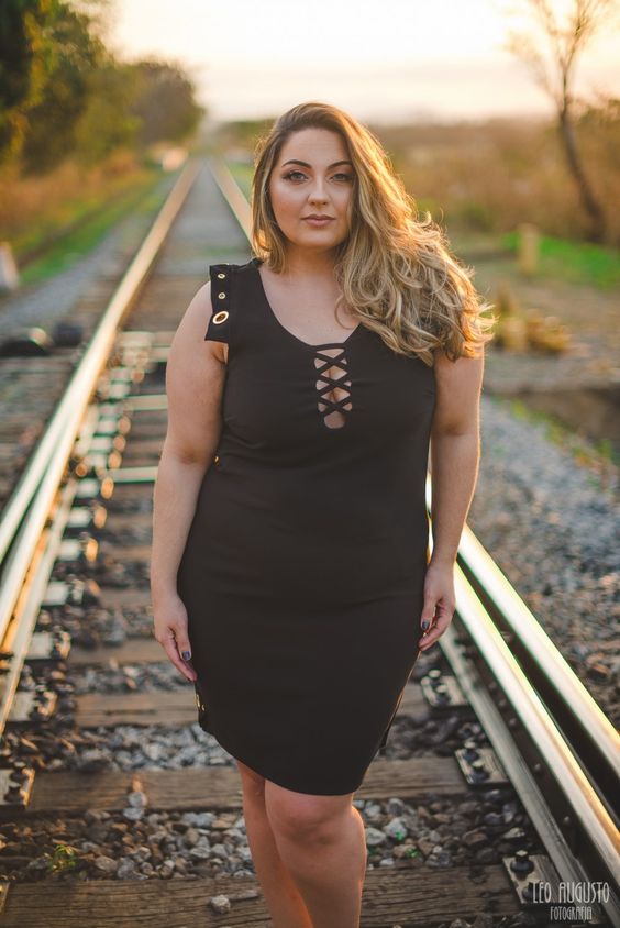 Mulheres gordinhas , representadas por  uma modelo, em foto na linha do trem com vestido elegante preto e bem penteada