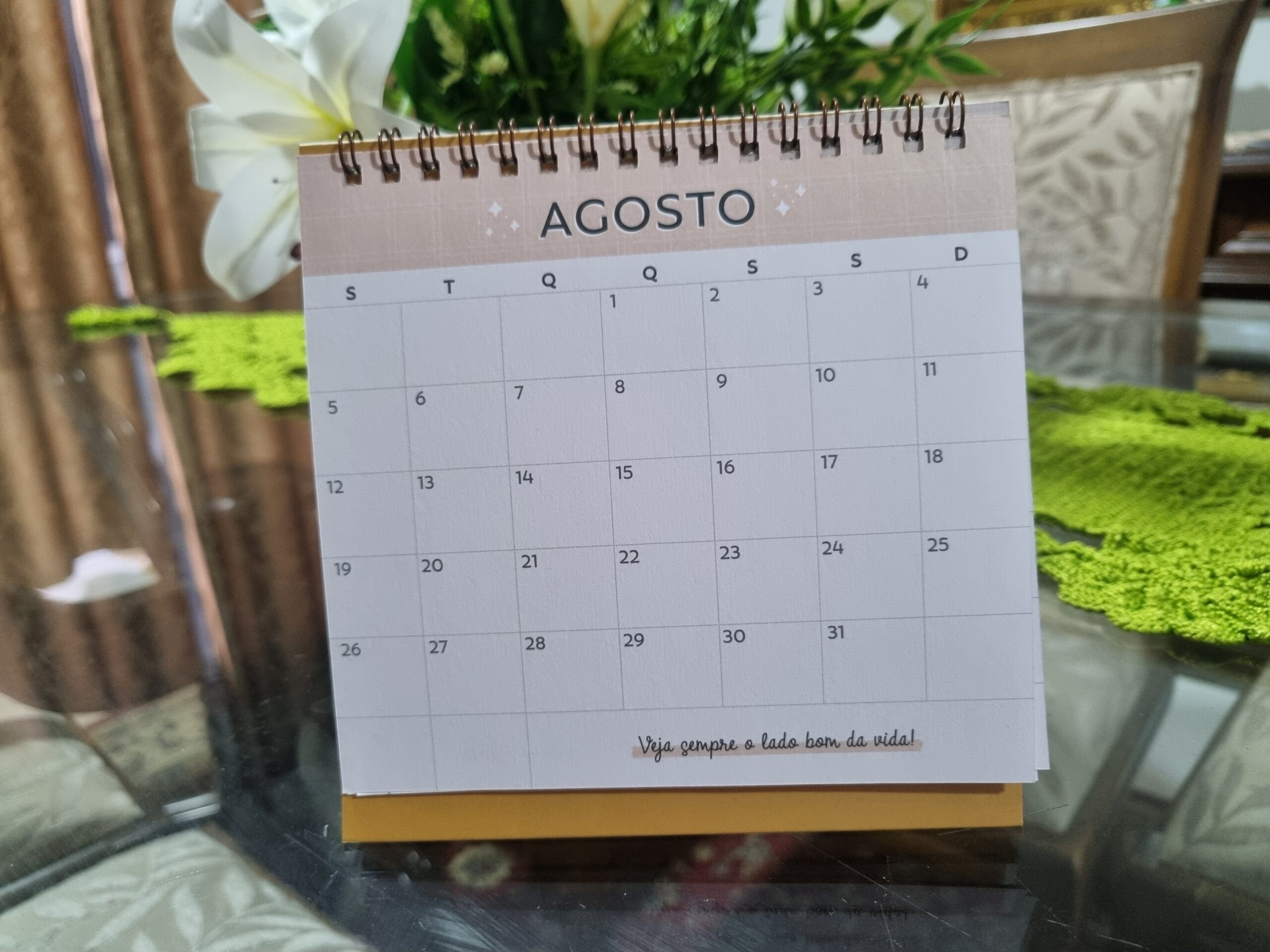 foto de uma calendário de mesa sobre uma mesa com detalhes de fundo com vaso de flor e toalha verde toalha na mesa de vidro